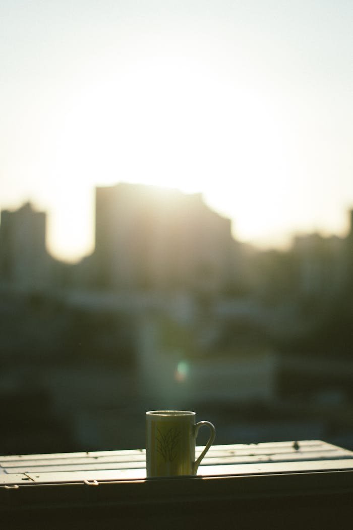 portfolio-img-04 A serene morning view with a coffee mug on a balcony against a blurred cityscape at sunrise.